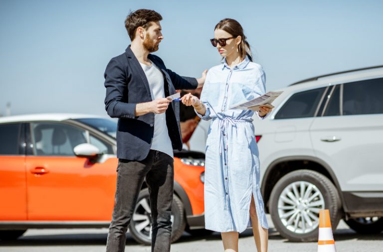 Man and woman arguing, standing together on the road with their cars on the background after the car accident