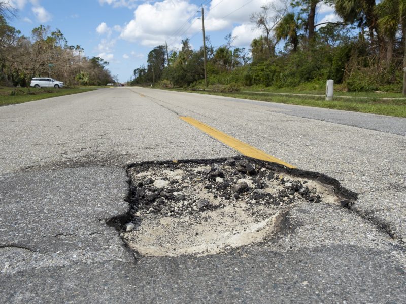 Damaged american road surface with deep pothole. Ruined street in urgent need of repair.