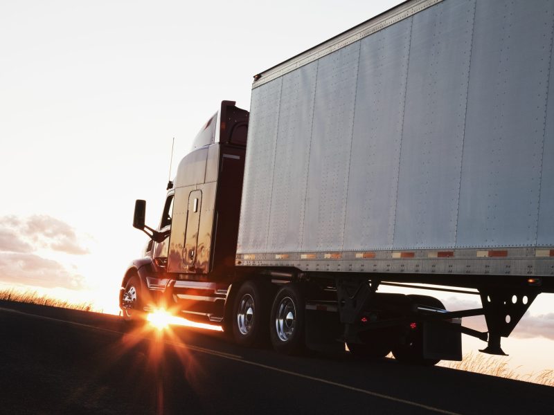 Silhouette of a  commercial truck driving on a highway at sunset.