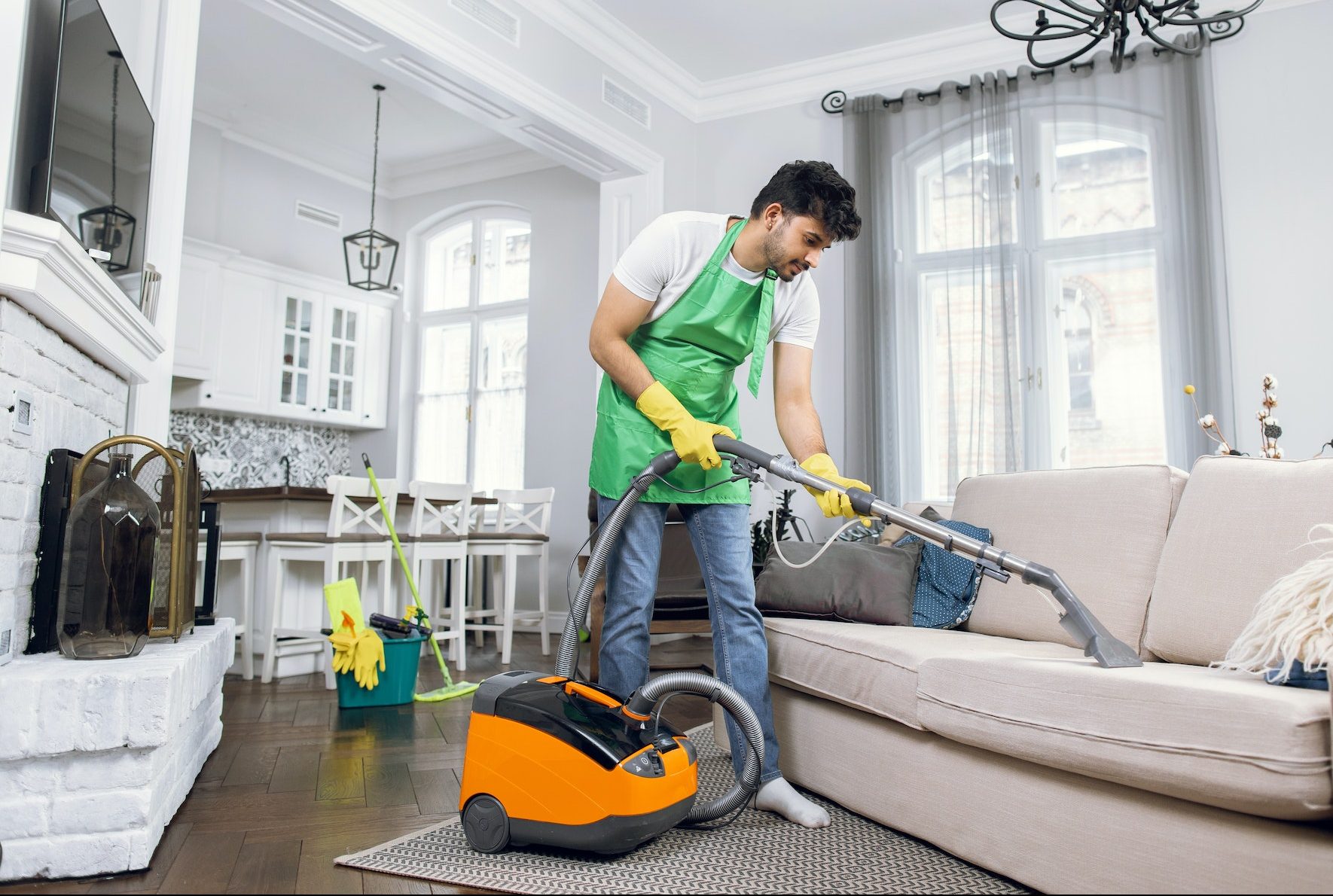 Indian male cleaner cleaning sofa with modern vacuum cleaner