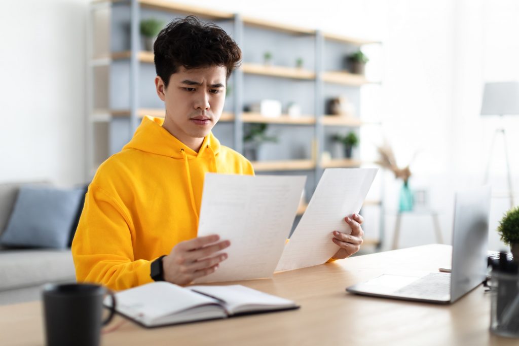 Man holding paper reading report working on laptop at home